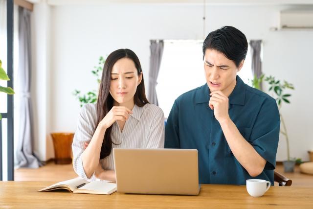 ノートパソコンを見ながら悩む夫婦