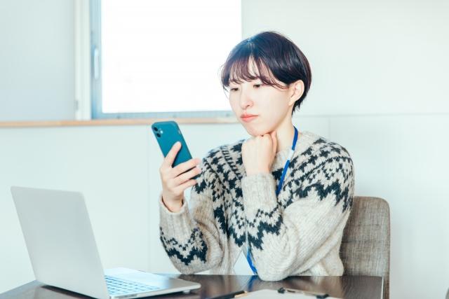 スマートフォンを見ながら考える女性