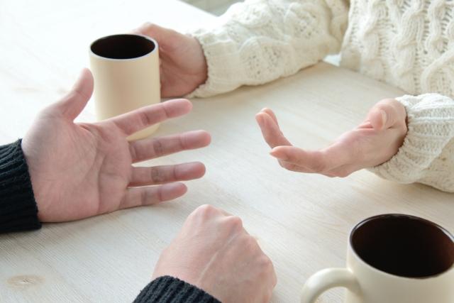 マグカップを前にテーブルで向かい合って話し合う二人の手元